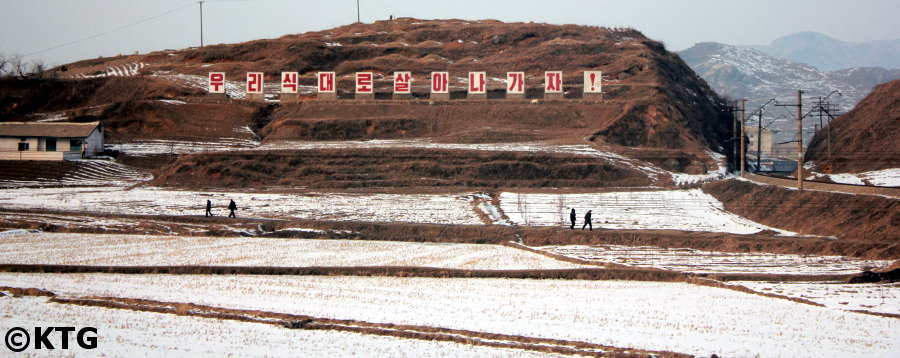 Campo en Corea del Norte en invierno con un eslogan gigante. Visite la RPDC con KTG Tours