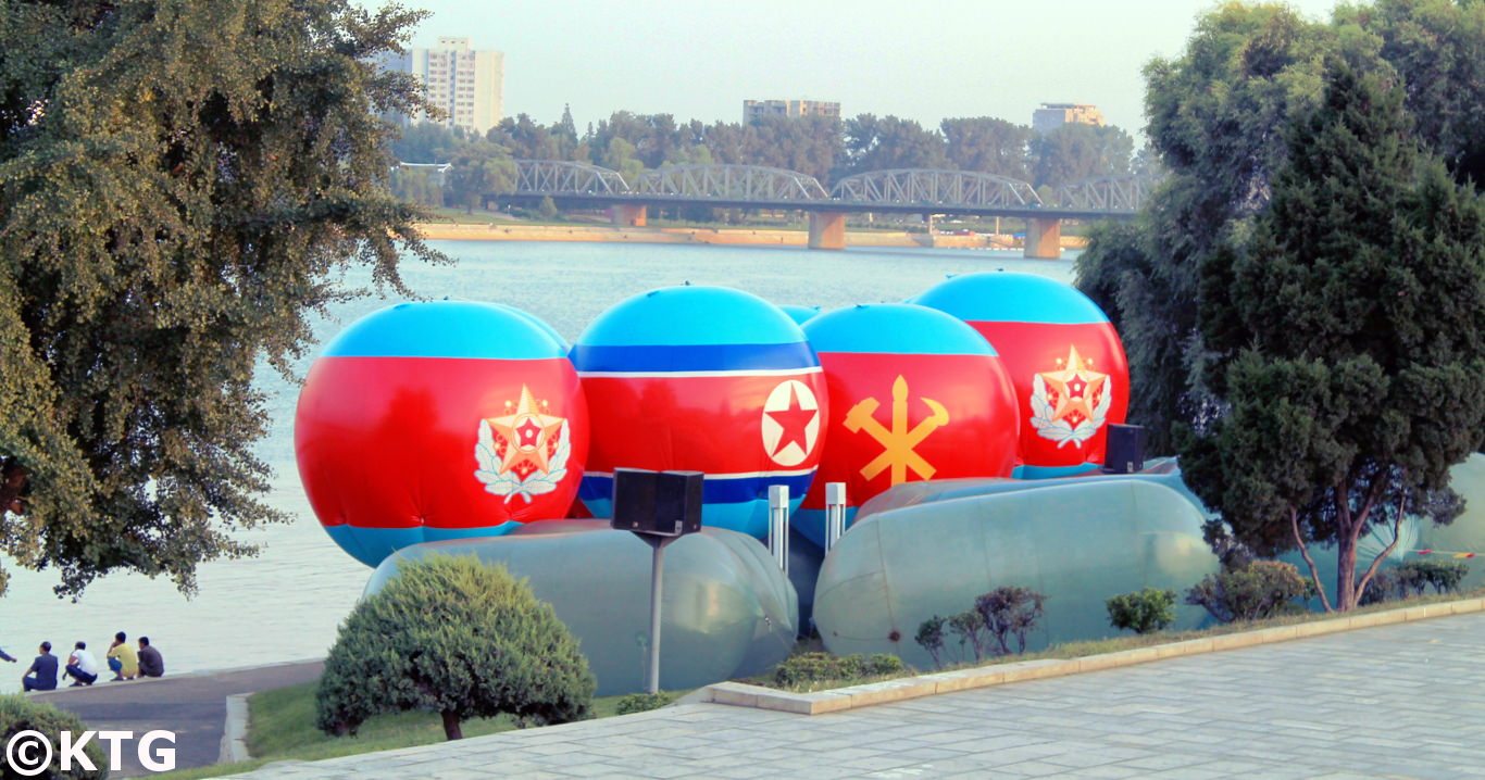 Imagen de la bandera de la RPDC y del símbolo del Partido de los Trabajadores de Corea en el medio de dos emblemas militares de la RPDC