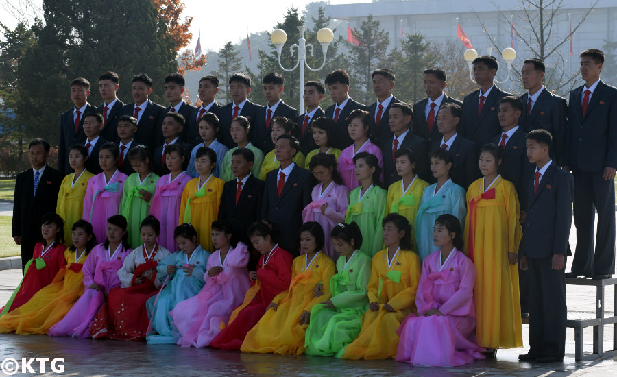Group of Koreans taking a group picture at the Kumsusan Palace of the Sun aka the Kumsusan Memorial Palace in Pyongyang in North Korea. This is the most sacred place in the DPRK. As you can see they wear formal clothes. Ladies wear traditional Korean dresses and men wear suit and tie or mao suits. Picture taken by KTG Tours