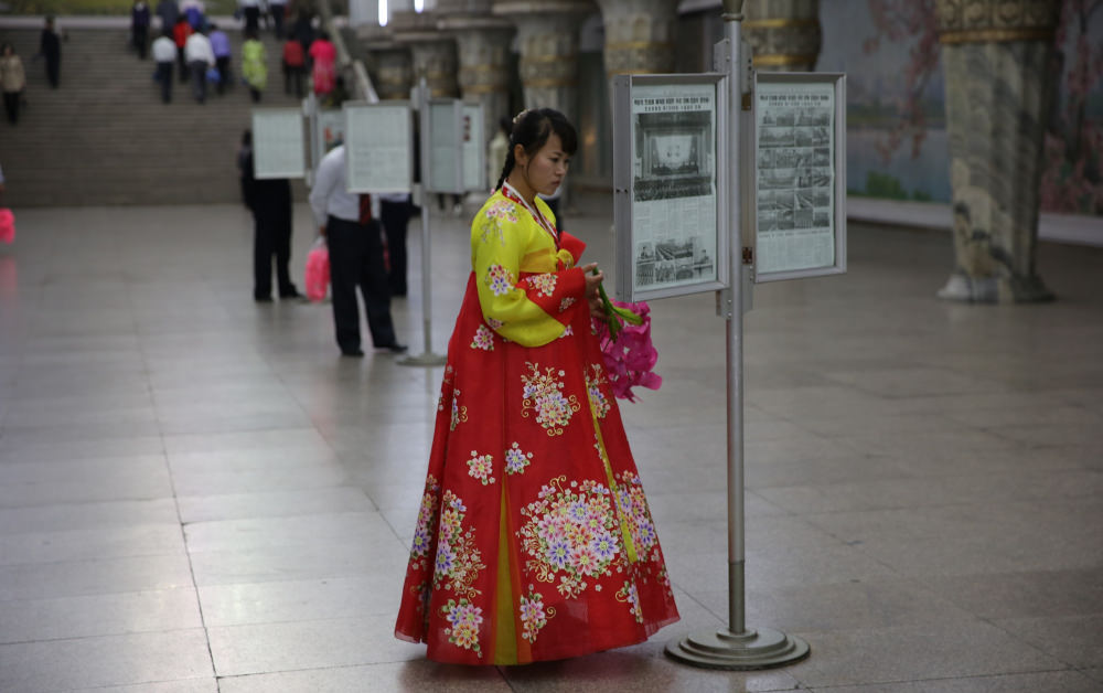 North Korean lady reading a framed newspaper in the Pyongang metro, DPRK