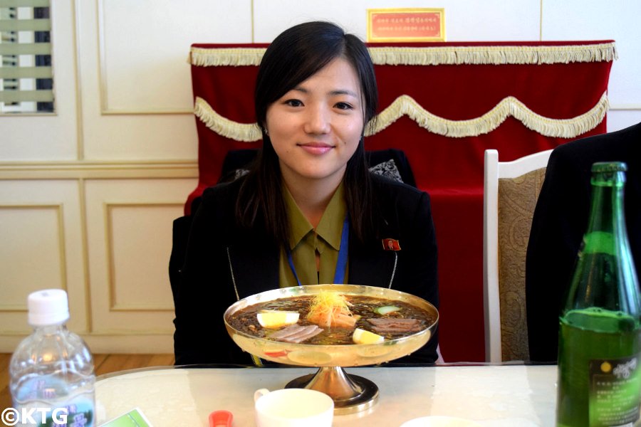 North Korean top guide Kim Sung Mi at the Okryu restaurant ie the Okryu-gwan or okryugwan with a bowl of cold noodles and a bottle of taedonggang beer in the capital of North Korea with KTG Tours