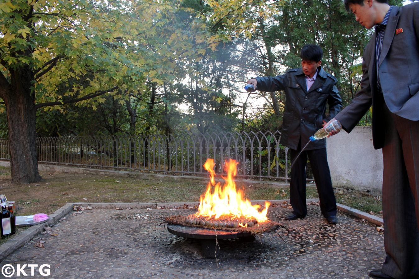 North Korean men pouring petrol over clams in order to prepare a clam barbecue. We can have a gasoline clam BBQ when staying at the Ryonggang Hot Spa Hotel in Onchon county near Nampo city on the west coast of North Korea, DPRK. Trip arranged by KTG Tours