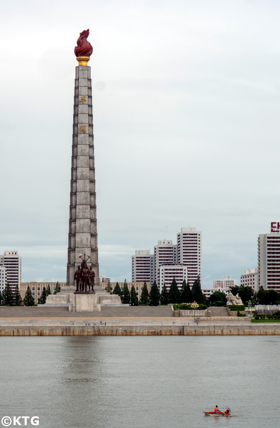 Couple en ramenant un bateau sur la rivière Taedong avec la tour Juche en arrière-plan. Voyage organisé par KTG Tours