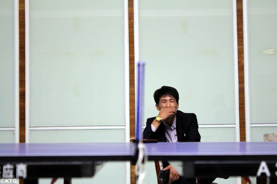 North Korean man laughing while watching a game of table tennis at the hot spa resort near Nampo city; The Ryonggang Hot Spa Hotel in North Korea, DPRK. Trip arranged by KTG Tours