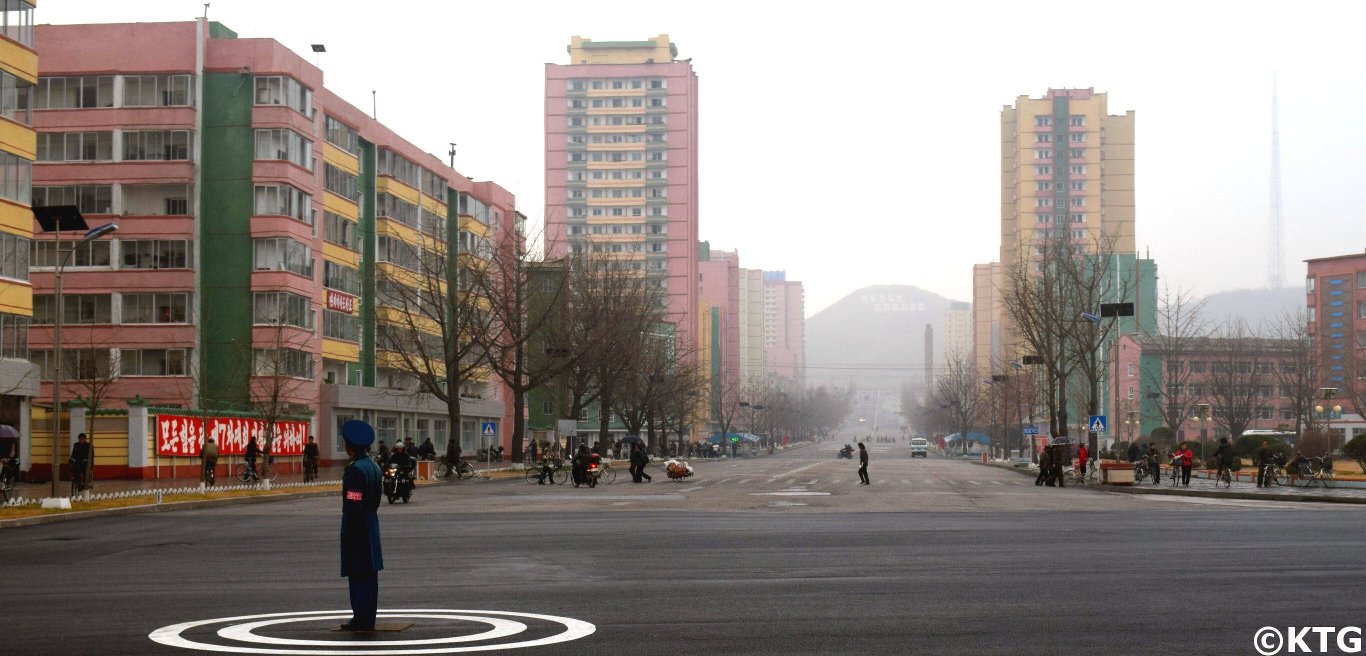 Agent de la police de la circulation nord-coréenne dans le centre-ville de Kaesong, Corée du Nord (RPDC). Vous pouvez voir les bâtiments emblématiques de grande hauteur en arrière-plan. Rejoignez KTG Tours pour explorer cette ville historique, qui abrite pas moins de 12 sites classés au patrimoine mondial de l'UNESCO