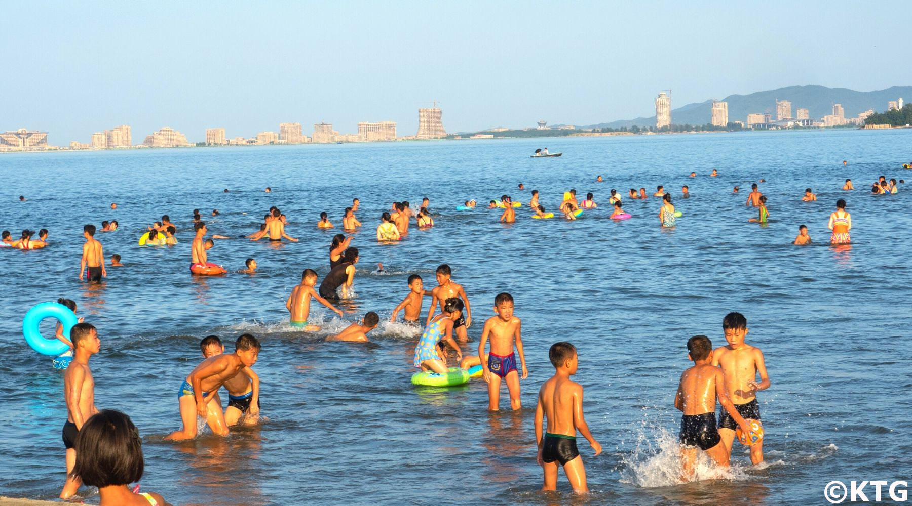Children having fun at the beach in Wonsan, North Korea. You can see the Wonsan-Kalma project in the background. Trip arranged by KTG Tours