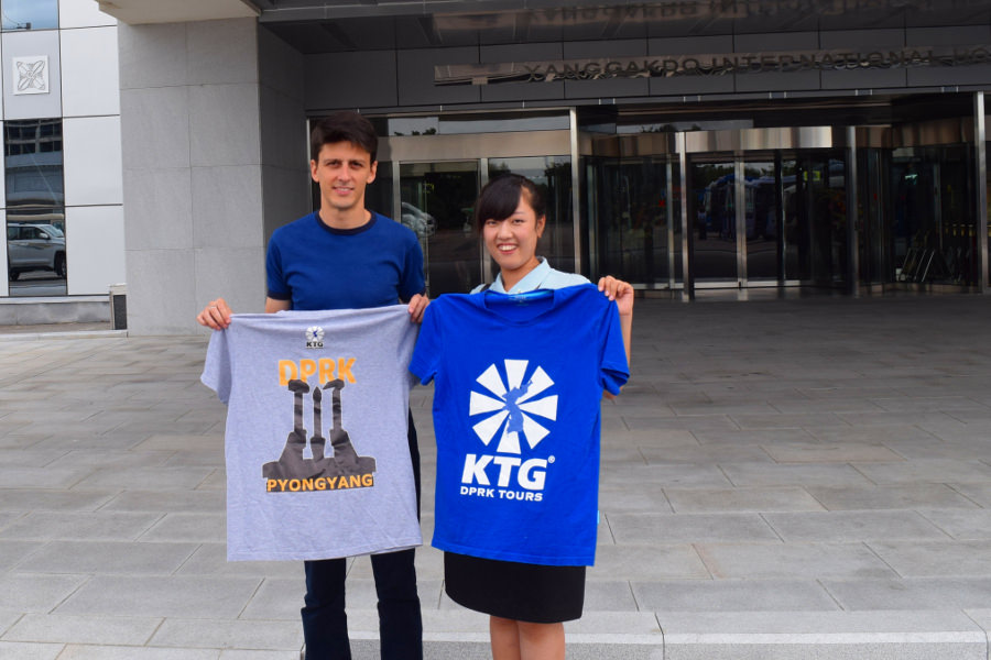 KTG staff member with North Korean guide, posing with KTG t-shirts, at the entrance of the Yanggakdo Hotel in Pyongyang, North Korea (DPRK)