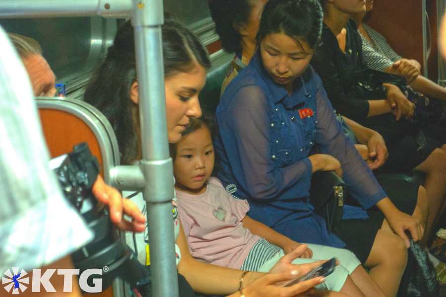 North Korean little girl playing with a traveller from KTG Tours on her mobile phone in the Pyongyang metro, DPRK